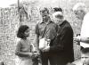 Archbishop Jordan holding a radio, speaking with a woman, child and mission voulnteer in Peru